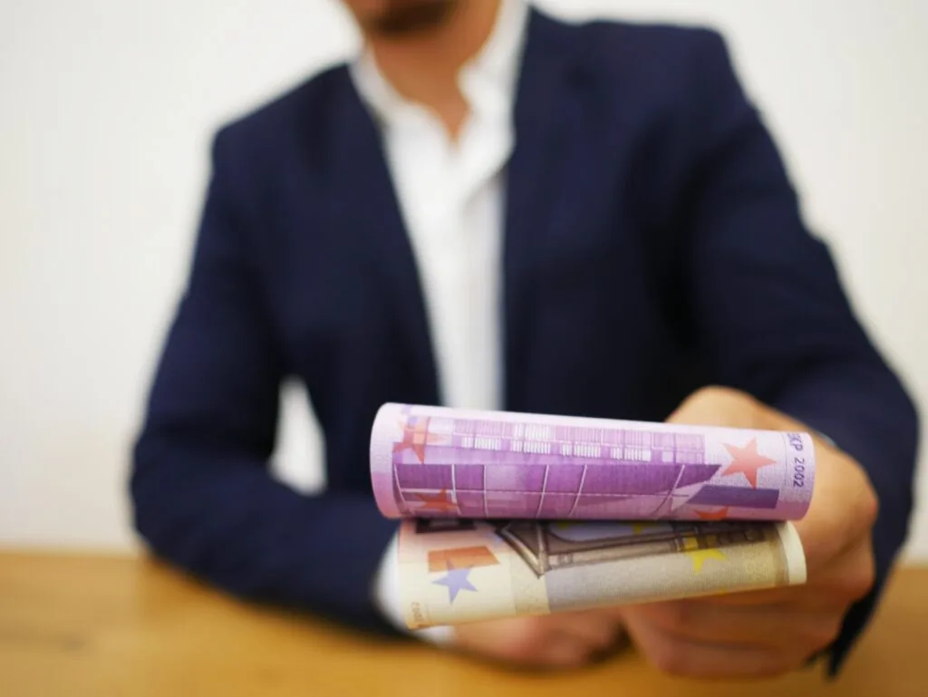 Bărbat oferind bancnote euro, simbolizând transparența salarială.