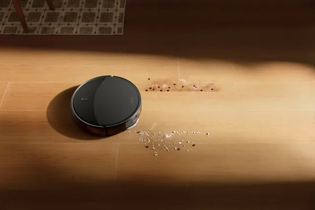 Robot aspirator curățând murdăria de pe podea.