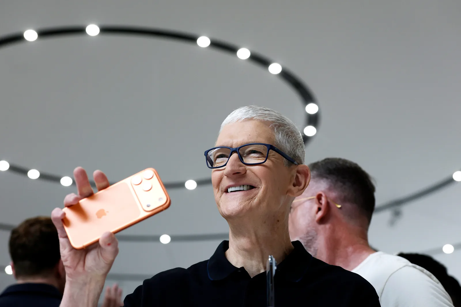 Tim Cook zâmbind în timp ce ține un telefon Apple în mână.