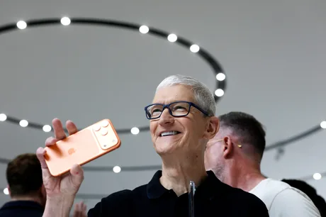Tim Cook zâmbind în timp ce ține un telefon Apple în mână.