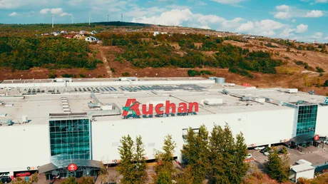 Clădire Auchan cu logo pe fațadă, înconjurată de natură.