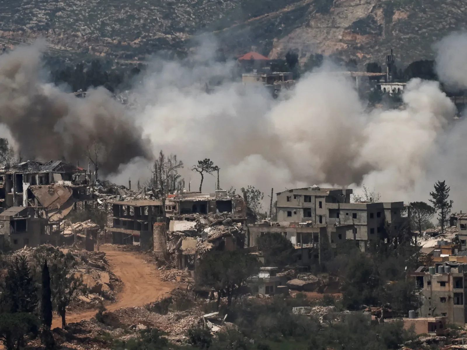 Peisaj distrus de război, cu clădiri în ruine și fum dens.