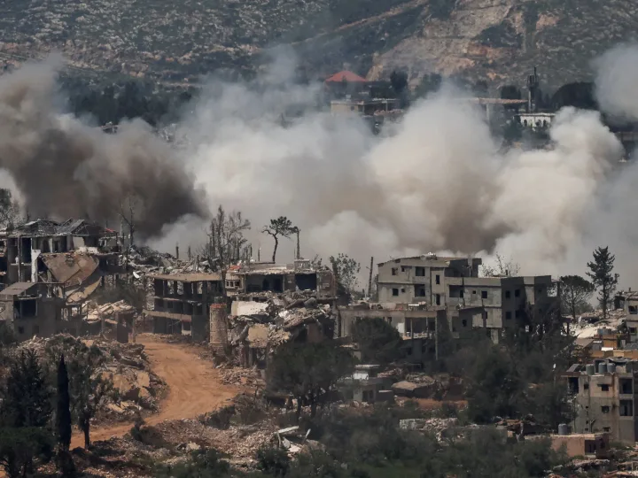 Peisaj distrus de război, cu clădiri în ruine și fum dens.