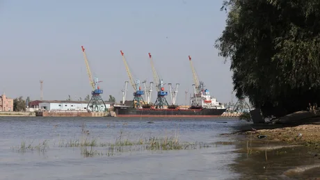 Vedere a unui port fluvial cu macarale și nave ancorate pe malul Dunării.