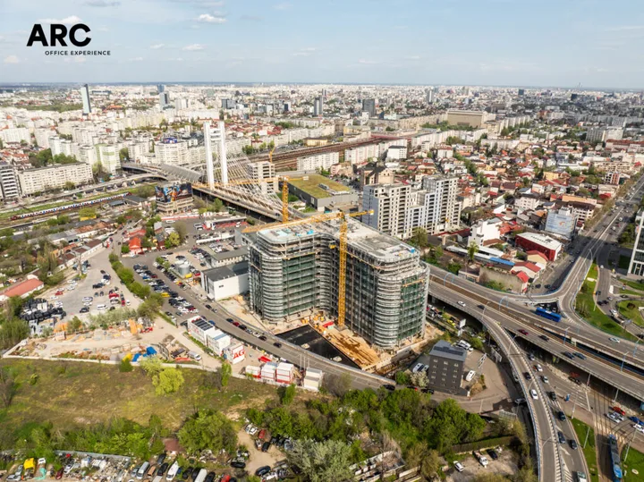 Clădire modernă de birouri în construcție, cu zone verzi și facilități pentru mobilitate urbană.