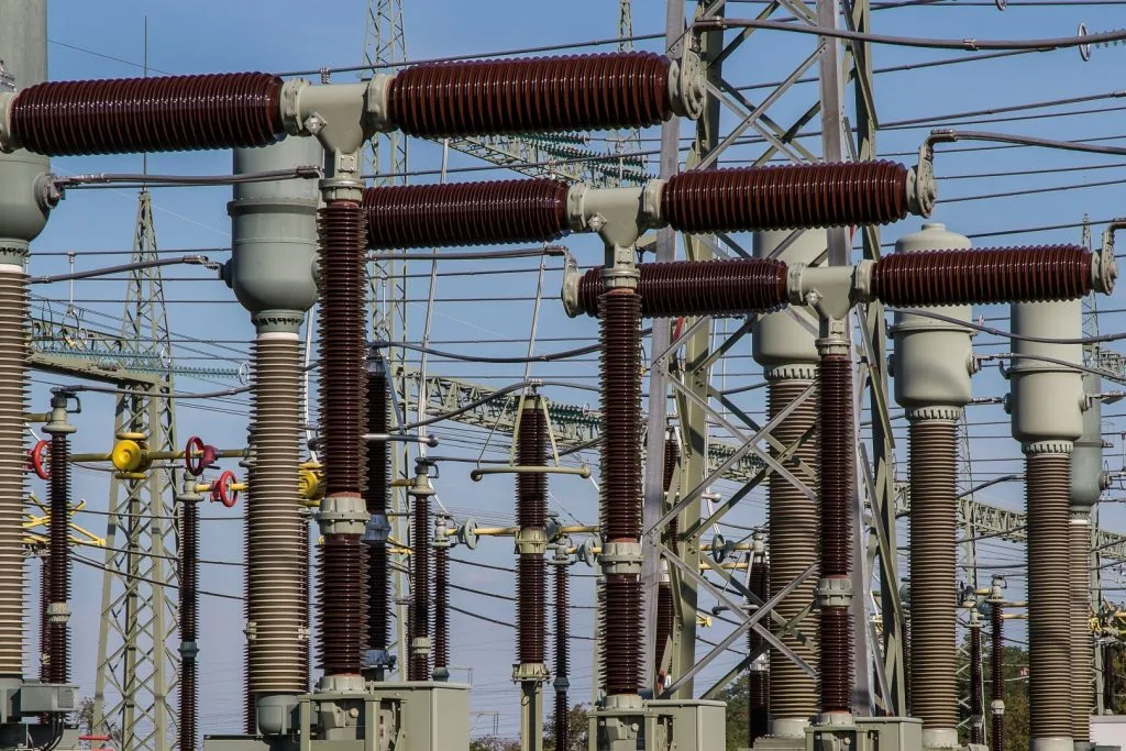 Echipamente electrice într-o stație de transformare, cu linii de înaltă tensiune în fundal.