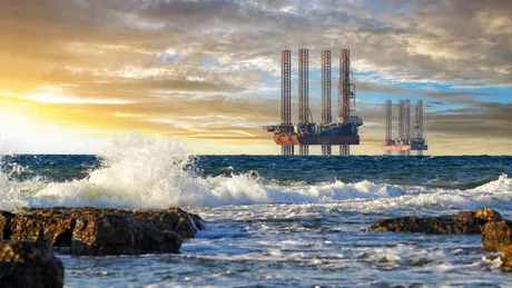 Peisaj maritim cu platforme de extracție și valuri spumoase.
