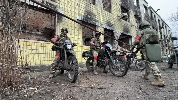 Soldați pregătiți pentru misiune în apropierea unei clădiri distruse.