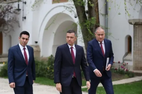 Trei politicieni discută în fața unei clădiri, purtând costume elegante.