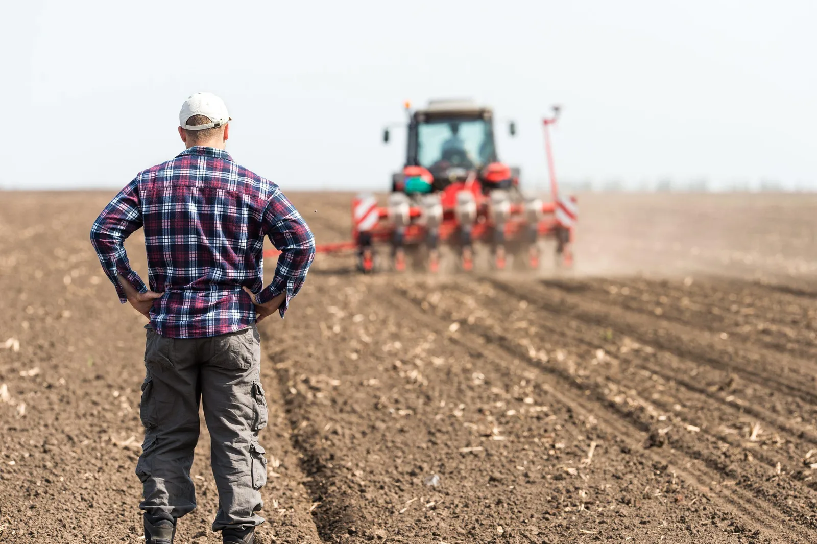 Fermier observând un tractor pe câmp în timpul lucrărilor agricole.