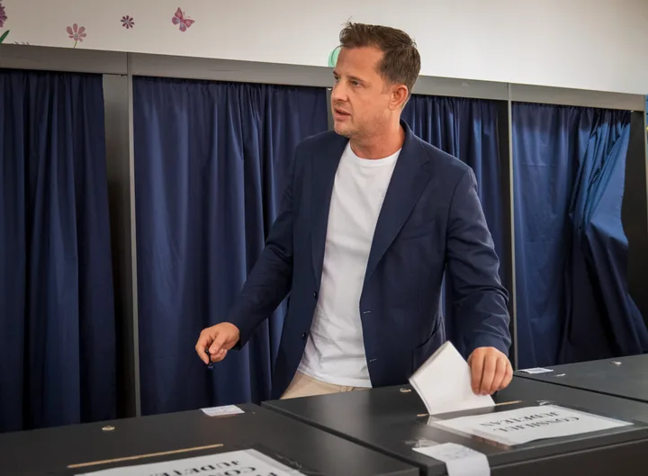 Bărbat la vot, într-un mediu electoral organizat, cu cabine de vot în fundal.