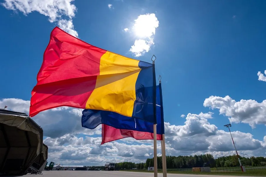 Steag românesc fluturând sub un cer senin cu nori pufoși.