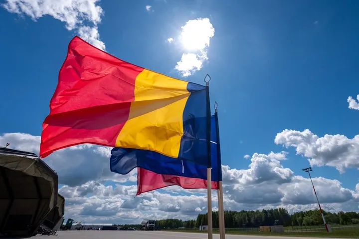 Steag românesc fluturând sub un cer senin cu nori pufoși.