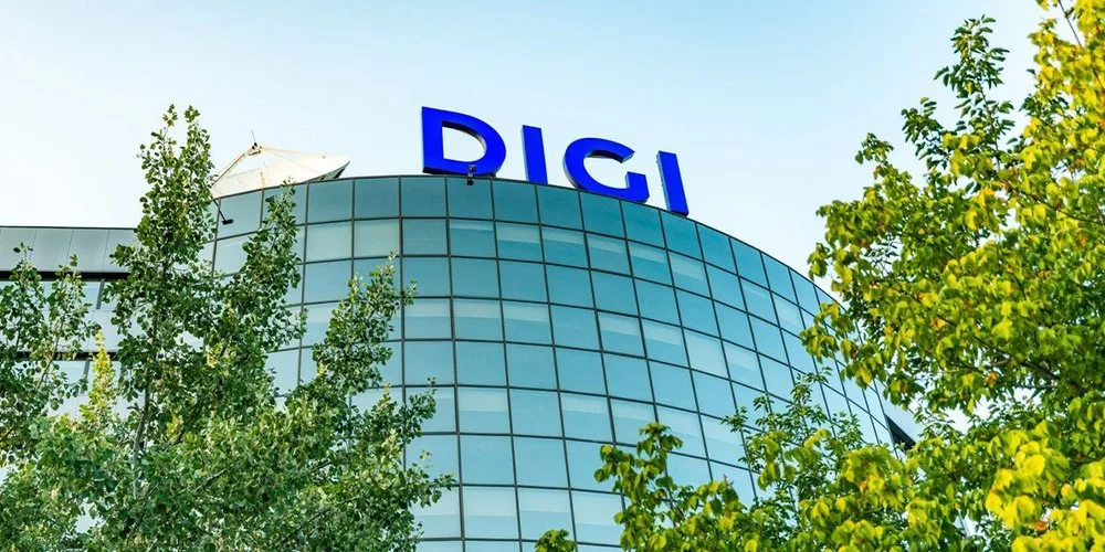 Clădire modernă cu logo Digi pe fațadă, înconjurată de copaci verzi.