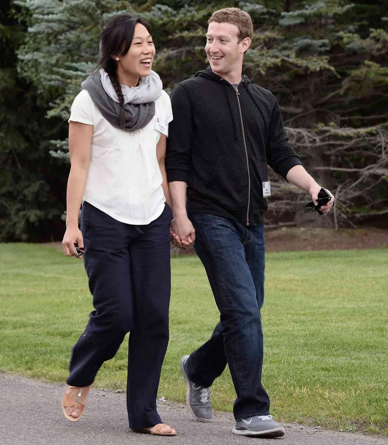 Mark Zuckerberg și Priscilla Chan plimbându-se pe o alee, zâmbind și ținându-se de mână.