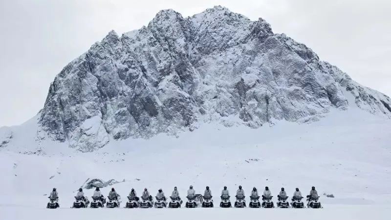 Trupe europene pe snowmobile în Groenlanda, în fața unui peisaj montan acoperit de zăpadă.