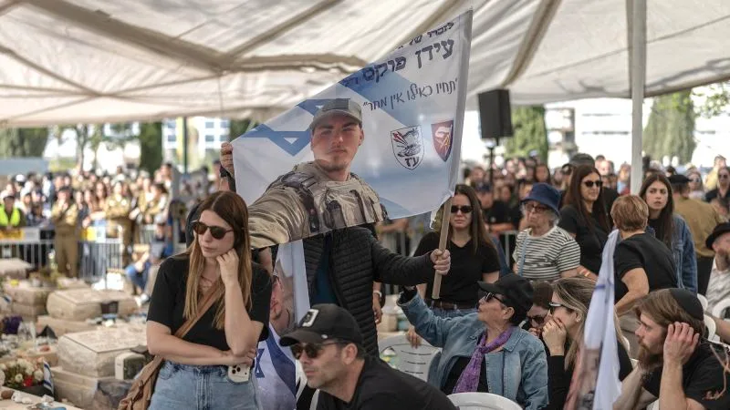 Oameni la o ceremonie, ținând steaguri și fotografii ale soldaților.