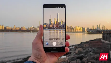 Un smartphone în mână, surprinzând un peisaj urban la apus, cu reflexii în apă.