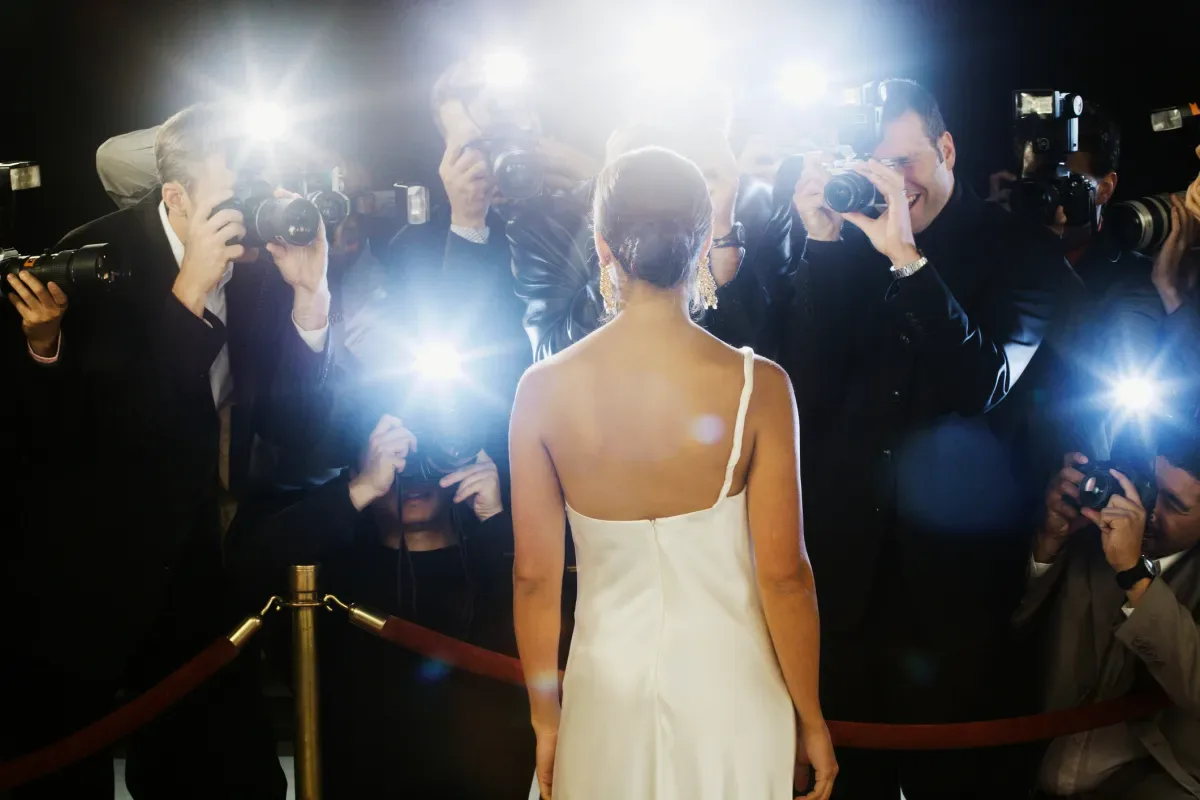 O celebritate în fața camerelor, înconjurată de fotografi flash.