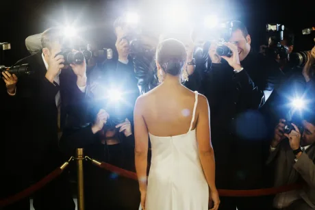O celebritate în fața camerelor, înconjurată de fotografi flash.