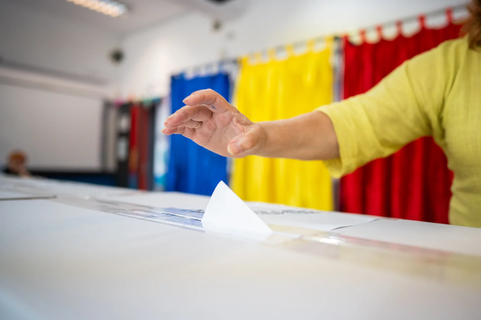 O persoană votează într-un birou electoral cu perdele colorate.