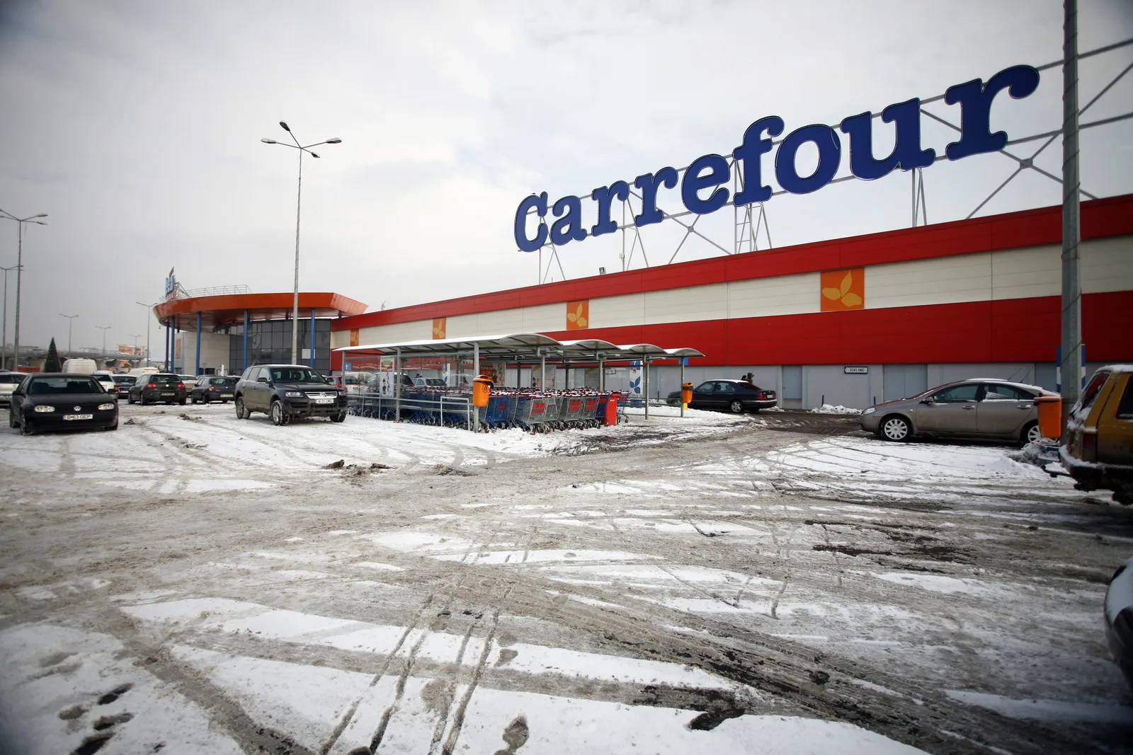 Magazin Carrefour înzăpezit, cu mașini parcate în față.
