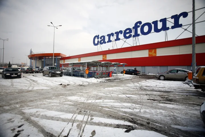 Magazin Carrefour înzăpezit, cu mașini parcate în față.