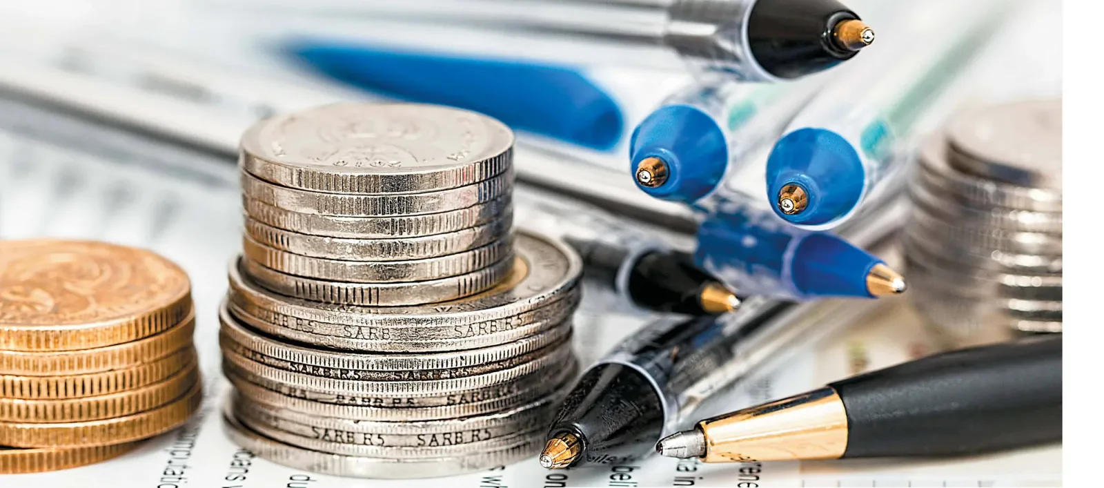 Monede și pixuri pe un birou, simbolizând economiile și investițiile.