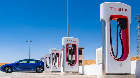 Stații de încărcare Tesla Supercharger într-o zonă deschisă, cu un vehicul alături.