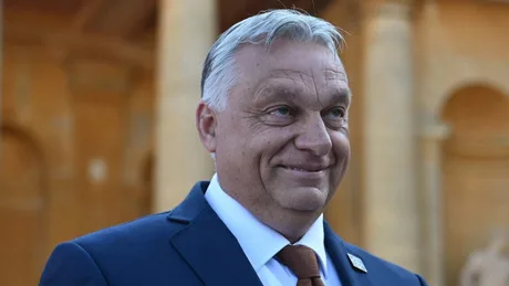 Viktor Orbán zâmbește în fața unei clădiri istorice, îmbrăcat elegant.