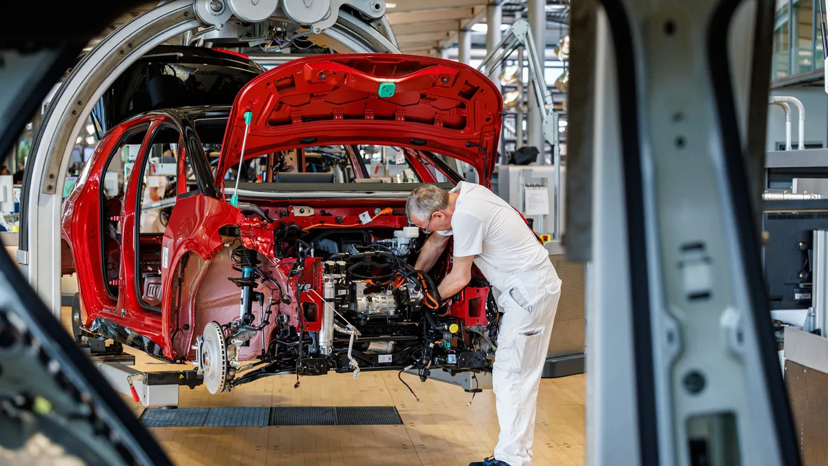 Muncitor în fabrică asamblează un automobil roșu.