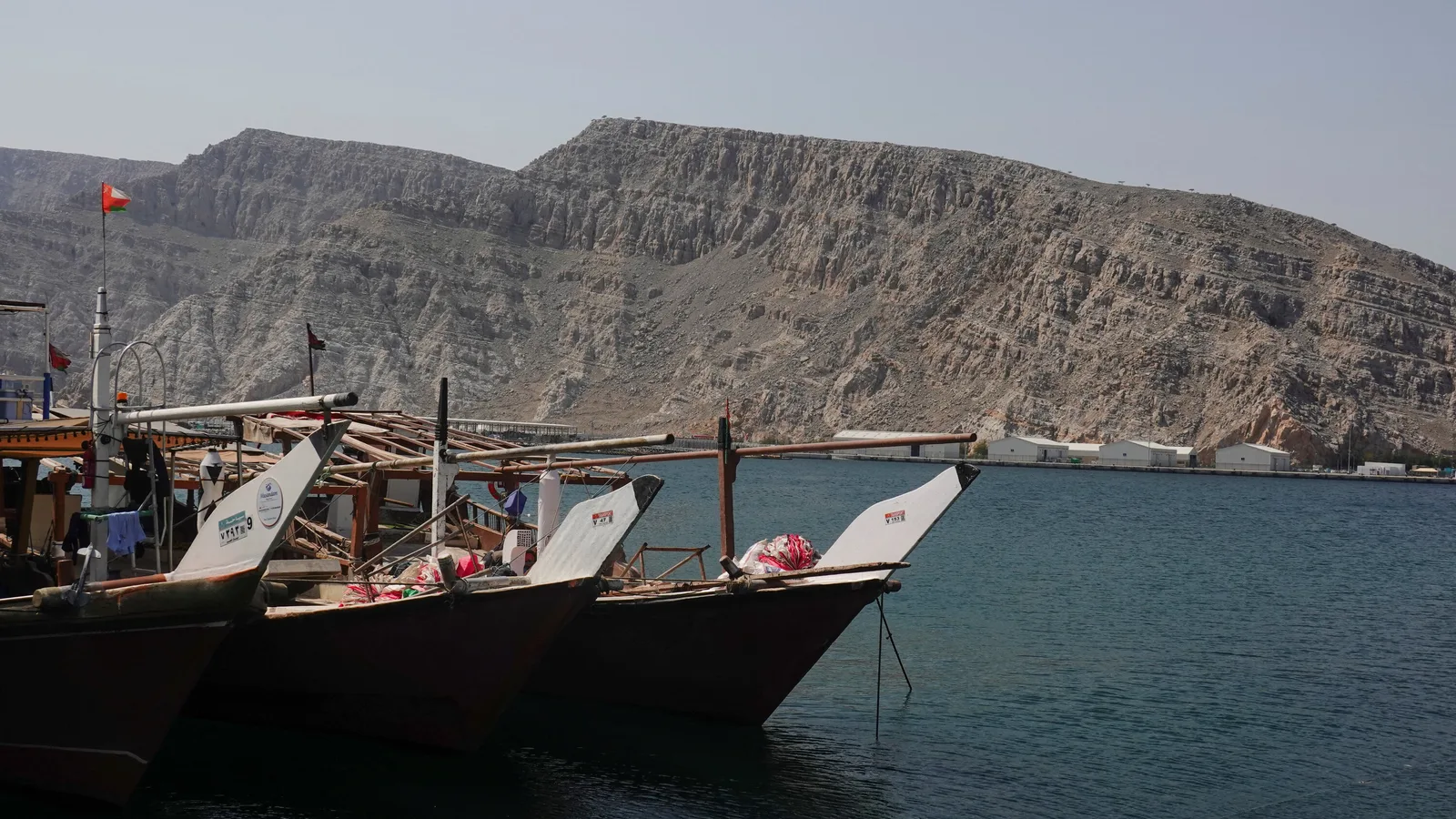 Bărcile ancorate în apă, cu munți în fundal, reflectă tensiunea din Golful Persic.