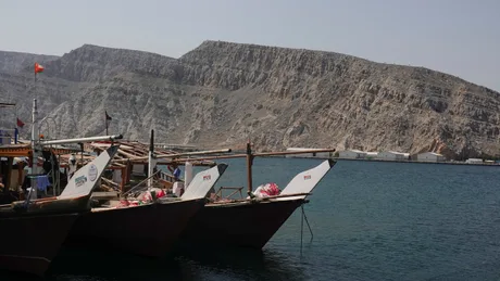 Bărcile ancorate în apă, cu munți în fundal, reflectă tensiunea din Golful Persic.