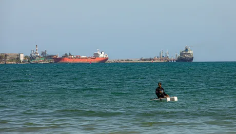 Un pescar pe apă, în fundal un petrolier în portul cubanez.