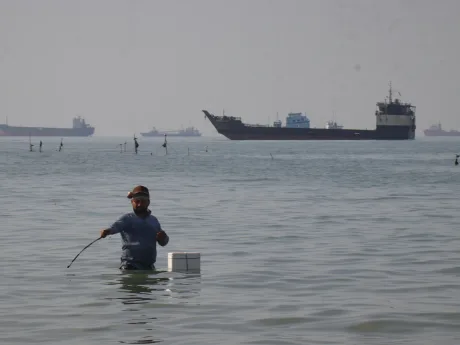 Un bărbat în apă, lângă o navă maritimă pe fundal.