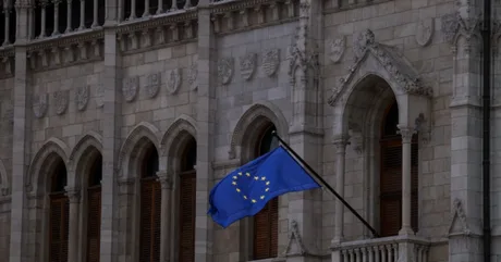 Clădire istorică cu steagul Uniunii Europene fluturând la fereastră.