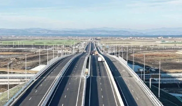 Vedere panoramică a autostrăzii în construcție, cu peisaj rural în fundal.