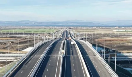 Vedere panoramică a autostrăzii în construcție, cu peisaj rural în fundal.