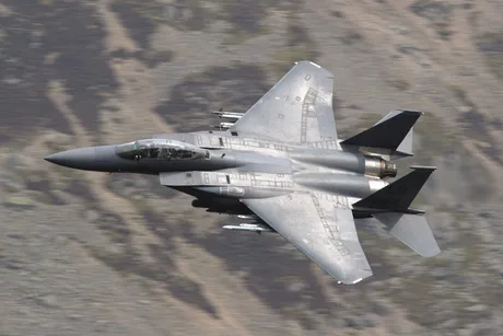 Avion militar zburând deasupra unui peisaj montan impresionant.