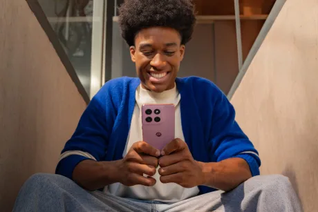 Un tânăr zâmbitor folosește un smartphone pe scări interioare.