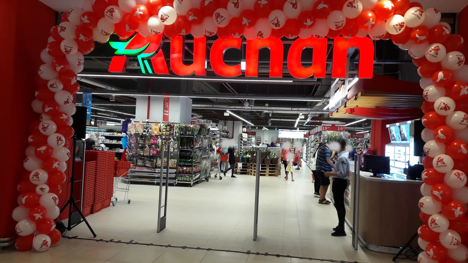 Intrarea unui nou supermarket Auchan, decorată cu baloane roșii și albe.
