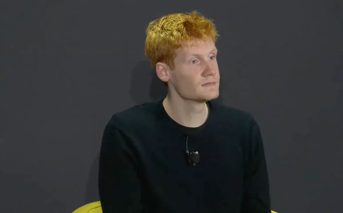 Un bărbat cu păr roșcat, îmbrăcat în negru, ascultând atent.