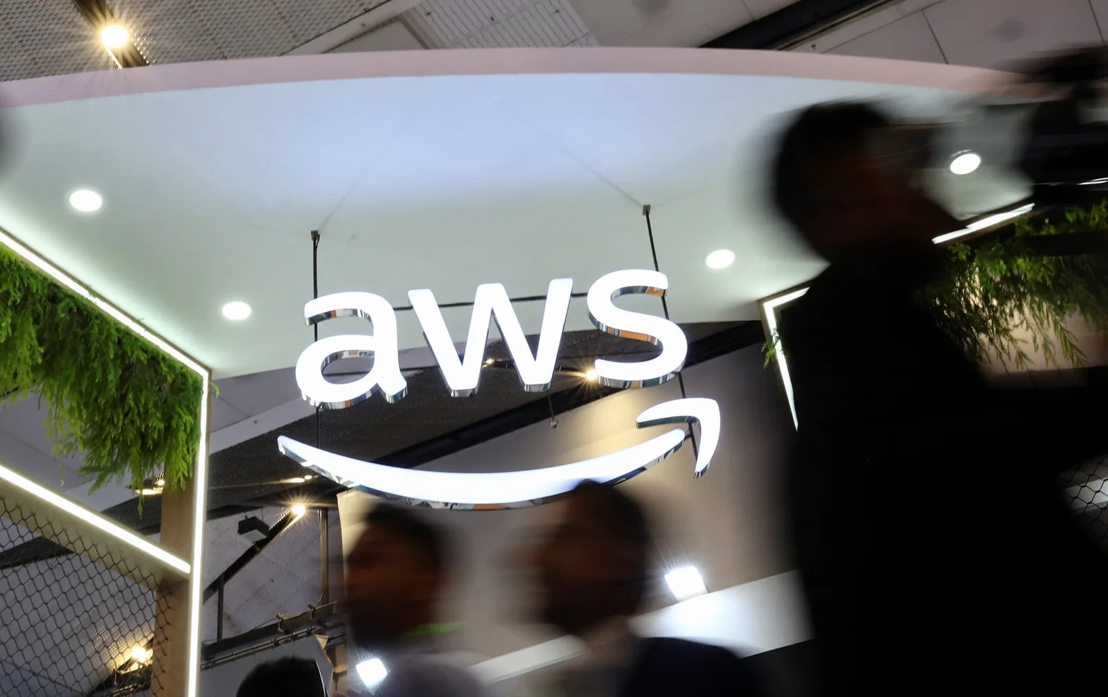 Logo AWS într-un mediu de expoziție, cu oameni în mișcare în fundal.