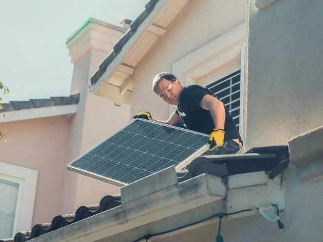 Un prosumator instalează panouri solare pe acoperișul unei case.