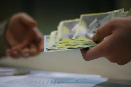 O persoană oferă bani în numerar, evidențiind problemele economice.
