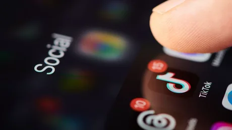 Un deget apasă pe un ecran de telefon cu aplicația TikTok deschisă.