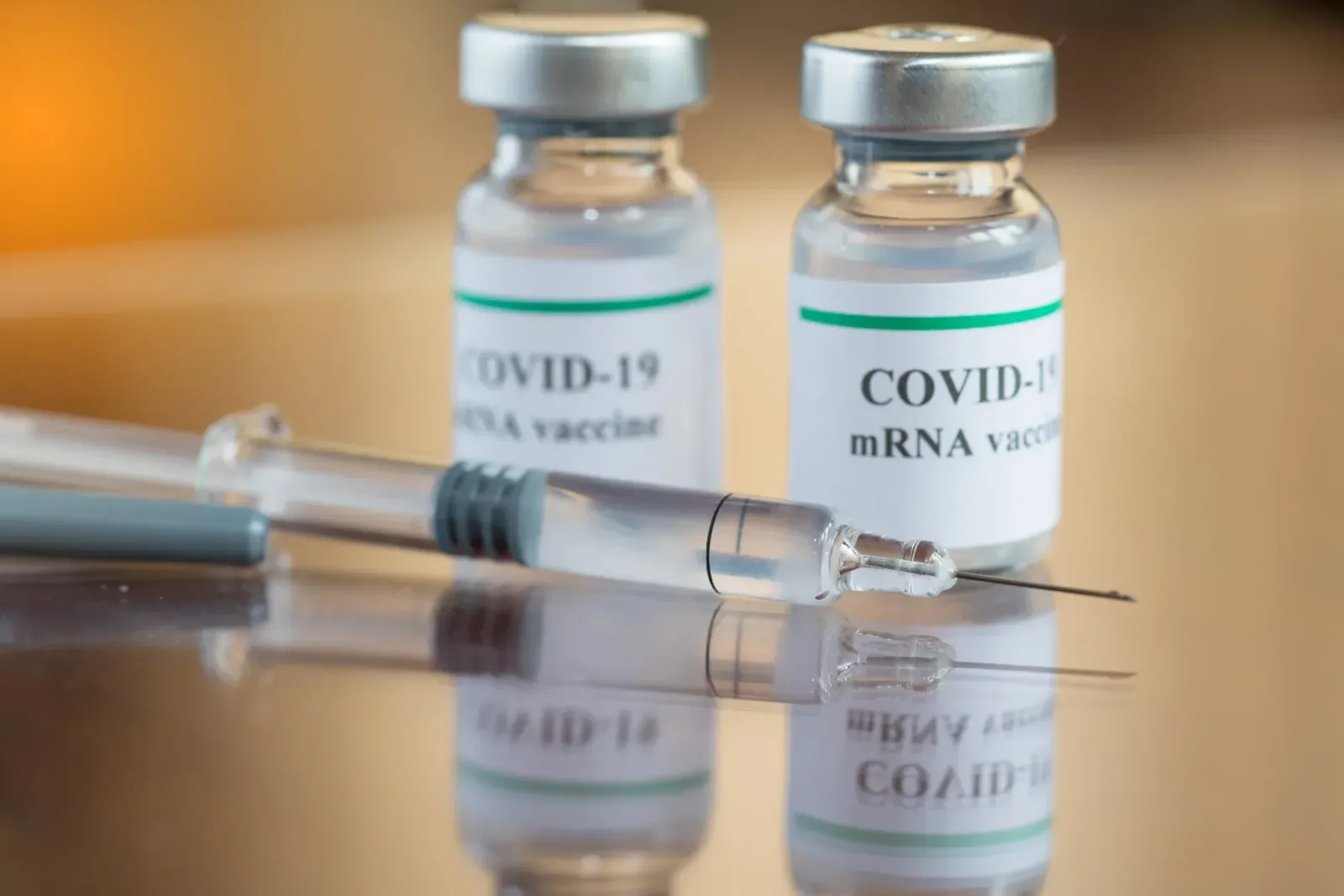 Flacoane de vaccin COVID-19 și o seringă pe o masă de lucru.