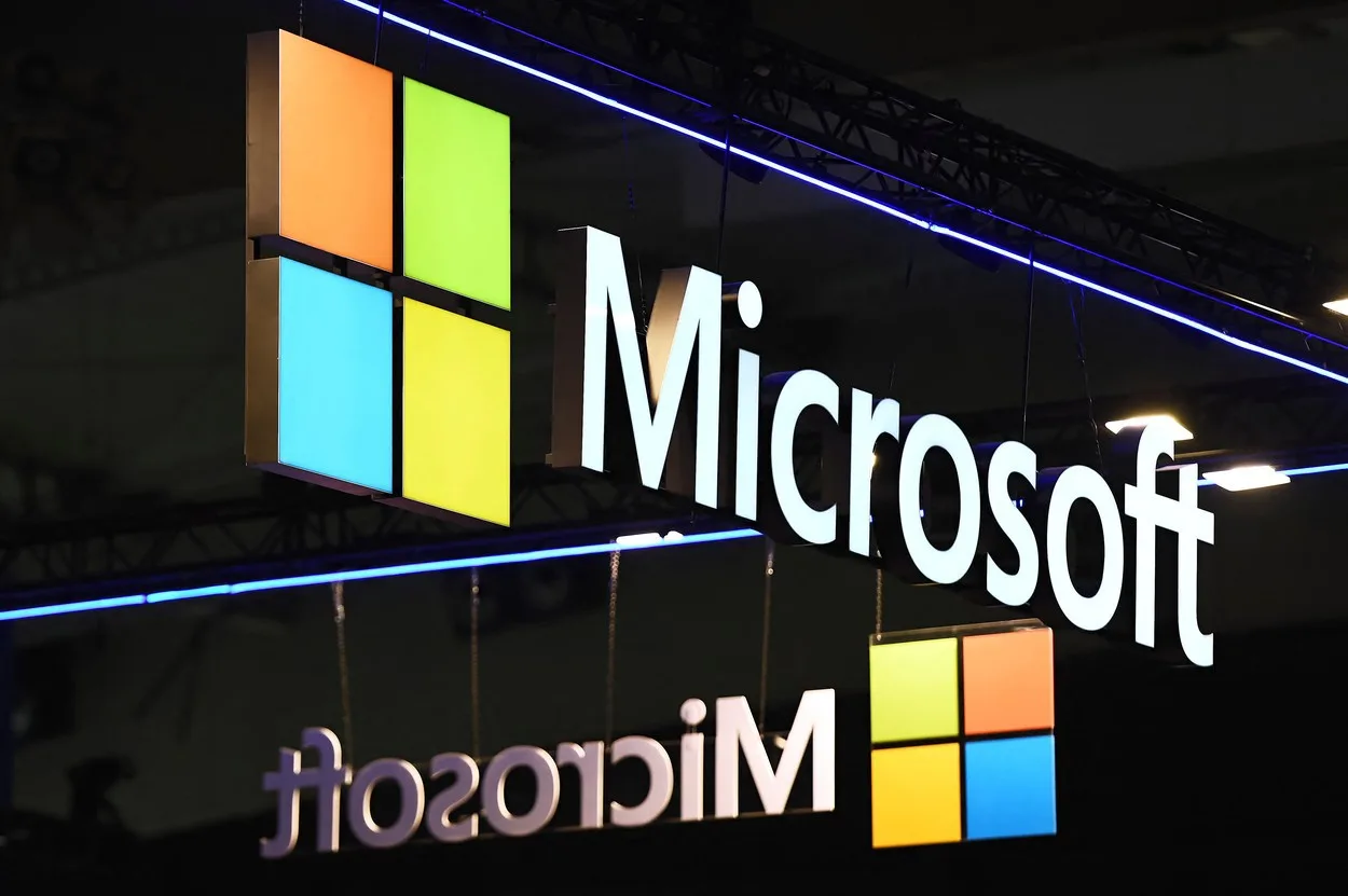 Logo-ul Microsoft suspendat pe un fundal întunecat, cu lumini colorate.
