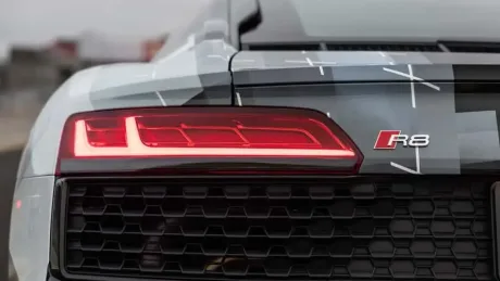 Detaliu al farurilor unui supercar Audi R8, evidențiind designul modern și tehnologia avansată.