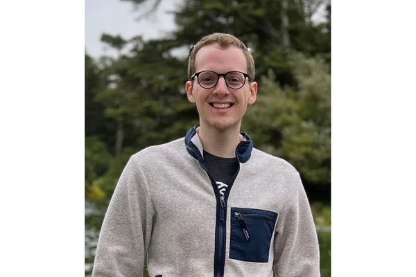 Bill Peebles zâmbind în natură, purtând o jachetă deschisă la culoare.